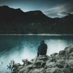 A person sits quietly by a calm lake embracing silence