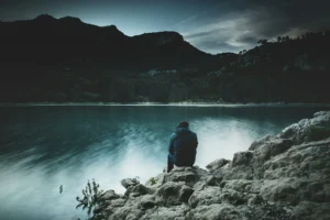 A person sits quietly by a calm lake embracing silence